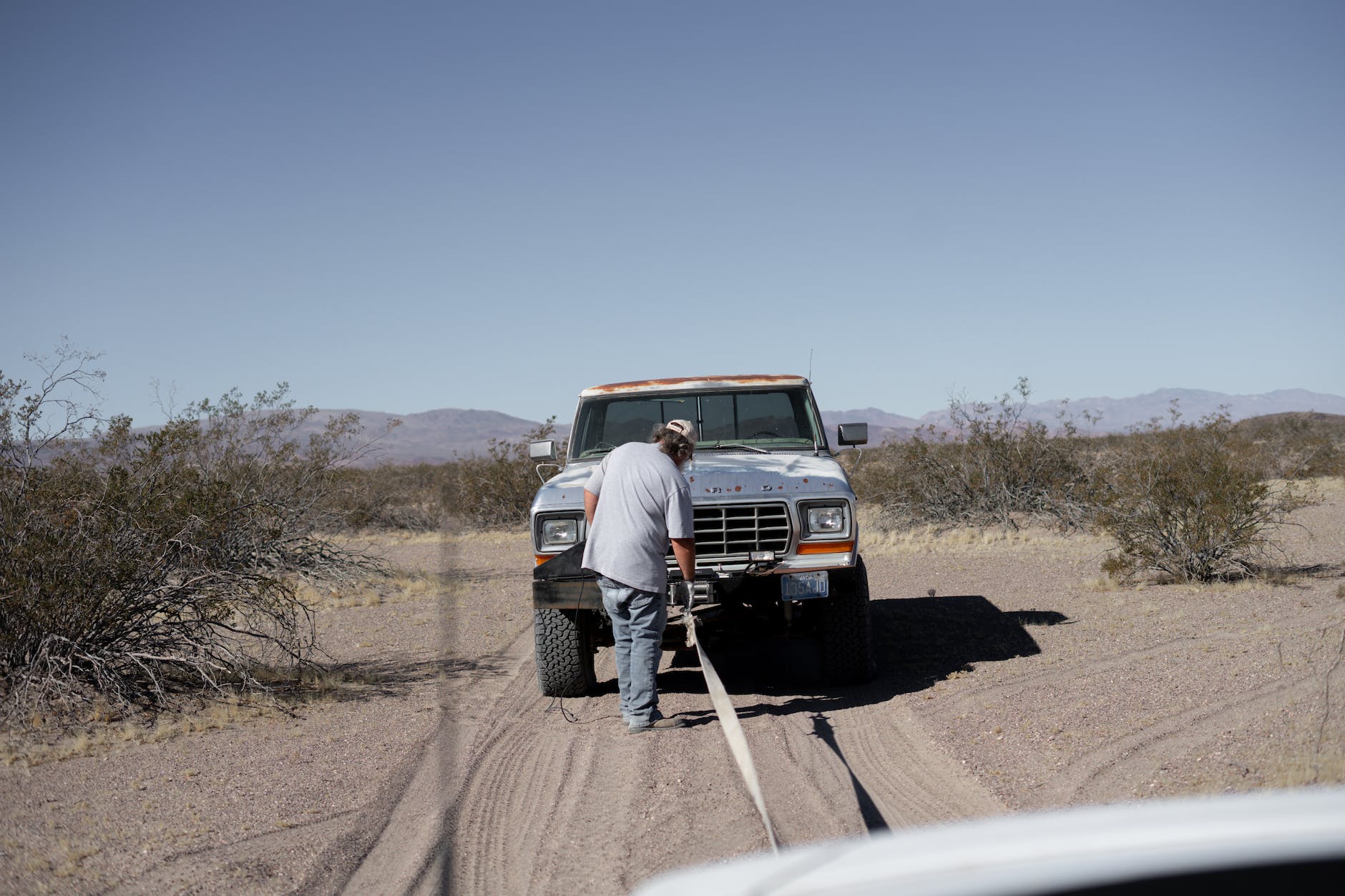 man towing a pick up truck on desert road